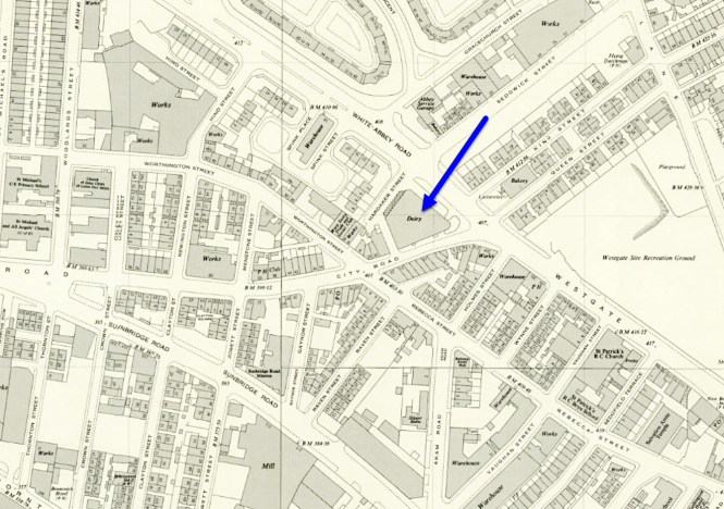 A historical Ordnance Survey map excerpt showing a dense urban and industrial sector, with a prominent blue arrow pointing down and to the left toward a building labeled "Dairy." The dairy sits at a major junction bordered by City Road, White Abbey Road, and Hardaker Street. Surrounding urban features include Worthington Street, Sunbridge Road, Westgate, several factories marked "Works," a playground, and the Westgate Site Recreation Ground.